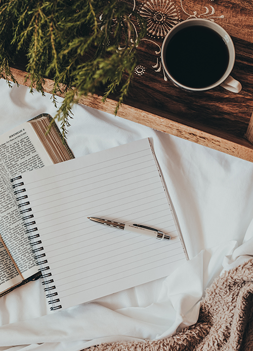 A photograph of a pen, notebook, and cup of coffee
