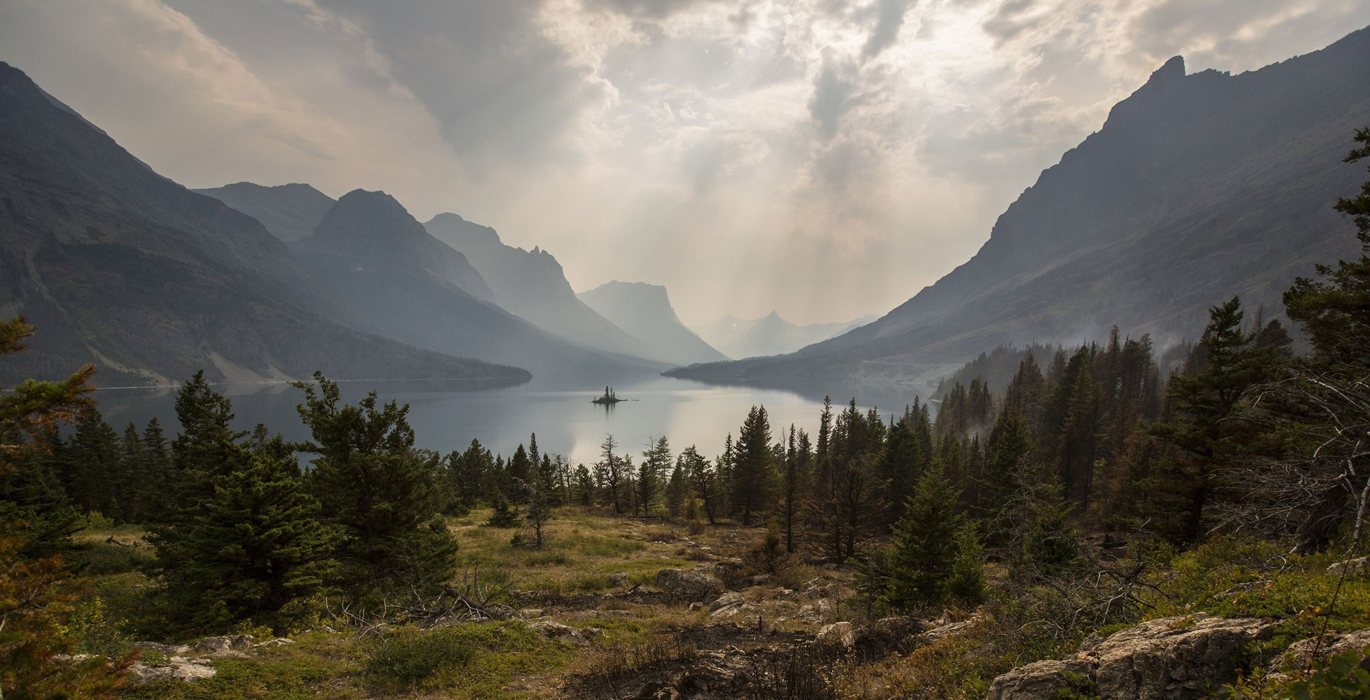 A photograph of a small lake surrounded by trees and mountains
